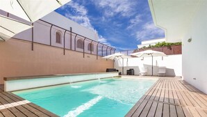 Ein Schwimmbecken mit Holzterrasse, weißen Sonnenschirmen und Liegestühlen.