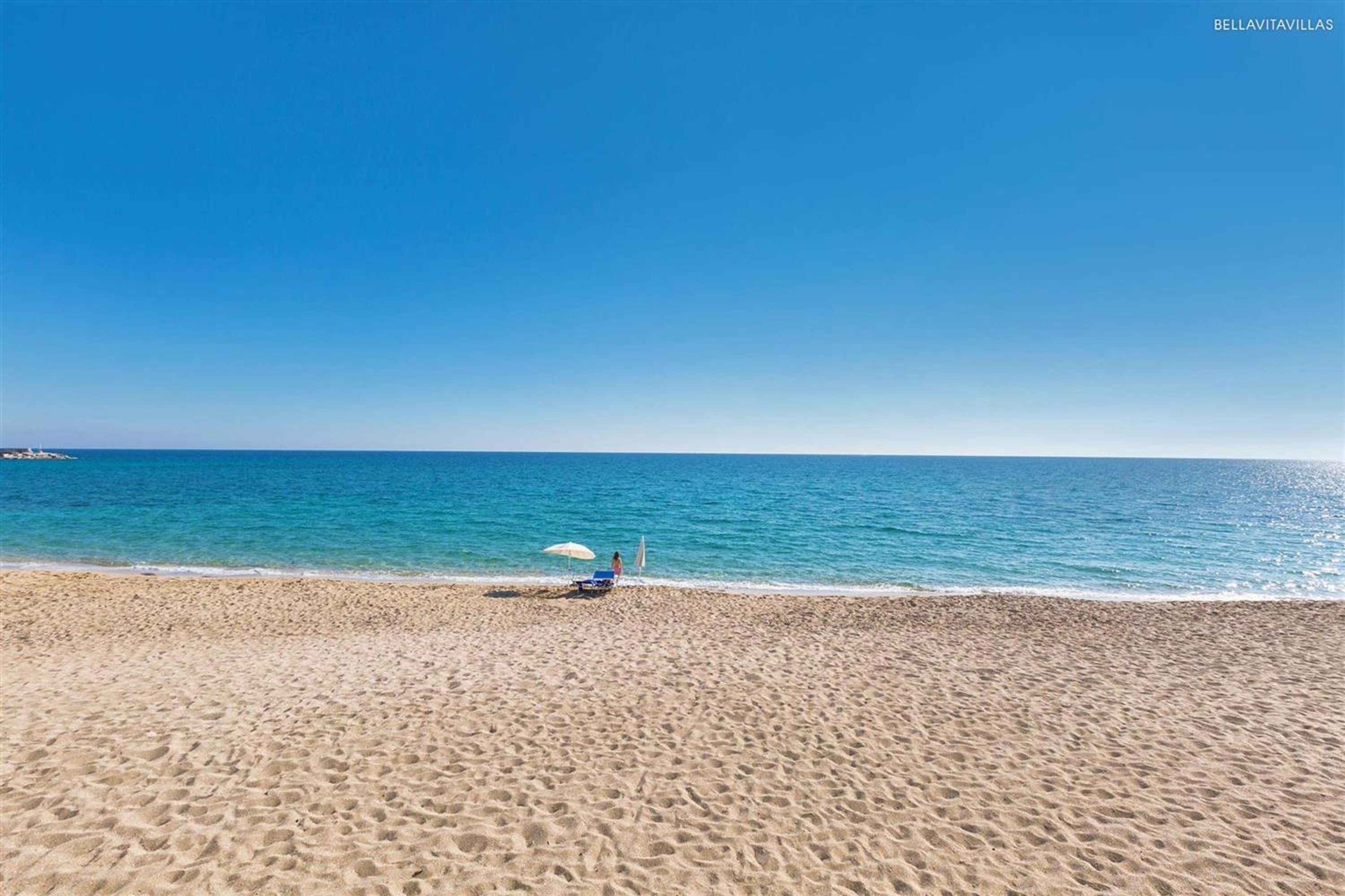 Une plage avec un ciel dégagé, une mer calme, un seul parasol et une seule chaise sur le sable.