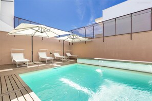 Ein Poolbereich auf dem Dach mit vier weißen Liegestühlen und zwei großen Sonnenschirmen.