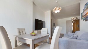 Ein modernes Wohnzimmer mit einer grauen Couch, einem Esstisch mit weißen Stühlen und einem flachbildfernseher an der Wand.