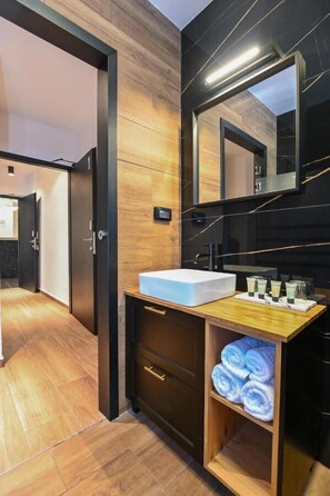 Une salle de bain moderne avec un meuble-lavabo en bois, un grand miroir et un lavabo. On y trouve des serviettes et des articles de toilette sur le meuble-lavabo.
