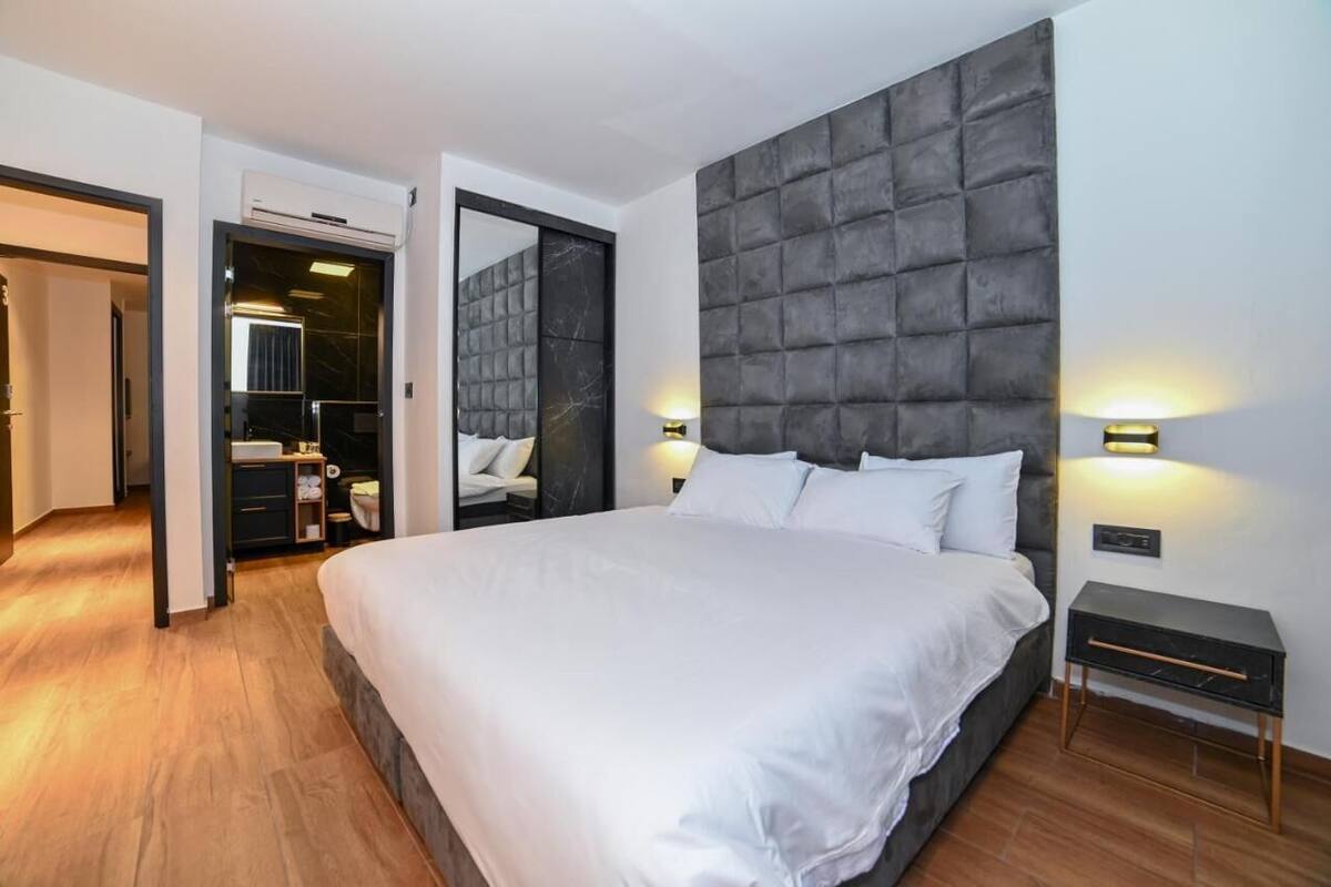 A modern bedroom with a large bed, a tufted headboard, bedside lamps, and a small bedside table.