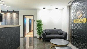 Een moderne receptie met een leren zwarte bank, een ronde tafel en een decoratieve wand met een logo.