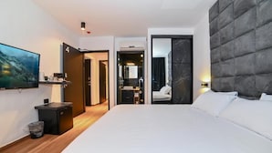 Een moderne hotelkamer met een groot bed, een flatscreen televisie, een klein bureau en een badkamer door een open deur zichtbaar.