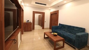 A modern living room with a blue sofa, wooden coffee table, and a TV on a wooden stand. - Seven Hills Hotels (Puri)