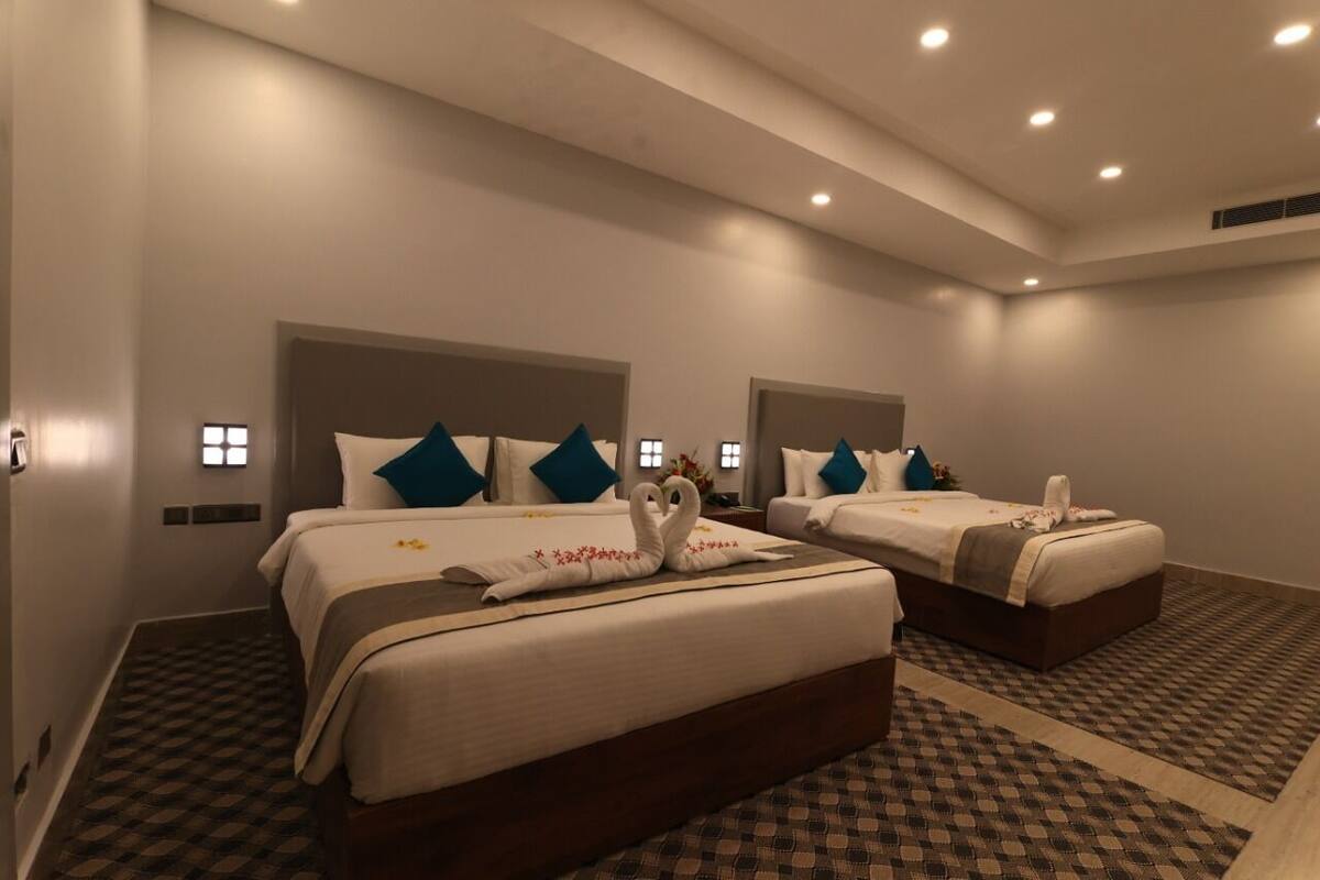 Habitación de hotel con dos camas, cada una con cabecera, ropa de cama blanca y almohadas decorativas.
