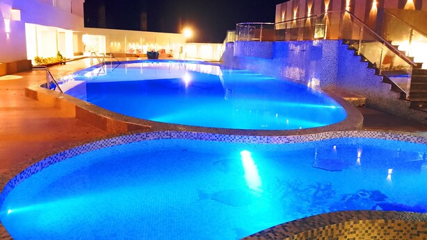 A swimming pool with a tiled edge, surrounded by a building with a staircase and illuminated walls. - Seven Hills Hotels (Puri)