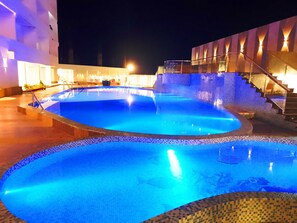 A swimming pool with a tiled edge, surrounded by a building with a staircase and illuminated walls. - Seven Hills Hotels (Puri)
