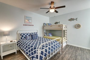 A bedroom with a bunk bed, a bedside table with a lamp, a ceiling fan, and a wall clock.