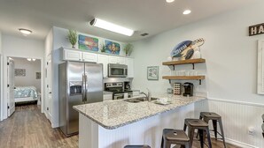 A modern kitchen with a granite countertop, stainless steel appliances, and a breakfast bar with stools. - New Listing: Peach Paradise (Port Aransas)