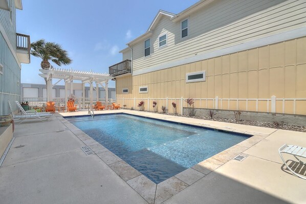 A rectangular swimming pool with lounge chairs and a pergola.