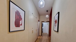 Un pasillo con suelo de madera, obras de arte enmarcadas en las paredes y una puerta al final.