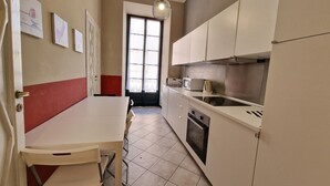 Una cocina compacta con armarios blancos, una pequeña encimera y un rincón comedor con una silla.