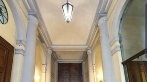 Un pasillo con piso estampado, un candelabro y una puerta doble de madera al final.