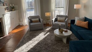 A living room with two grey sofas, a blue sofa, a round coffee table, and a fireplace. - Charming renovated historic home in ideal location (Hamilton)