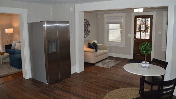 A modern living room with a large stainless steel refrigerator, a beige sofa, a round dining table with two chairs, and a small potted plant. - Charming renovated historic home in ideal location (Hamilton)