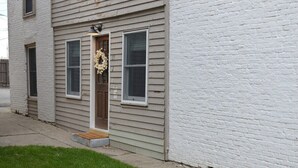 A two-story house with a front door, a small porch, and a white brick wall. - Charming renovated historic home in ideal location (Hamilton)