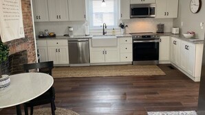 A modern kitchen with white cabinets, stainless steel appliances, and a dining area with a table and chairs. - Charming renovated historic home in ideal location (Hamilton)