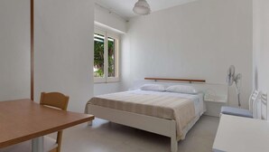 A bedroom with a bed, bedside table, and a window with a view of greenery. - 674 Villetta con Vista Mare a Santa Maria al Bagno (Nardò)