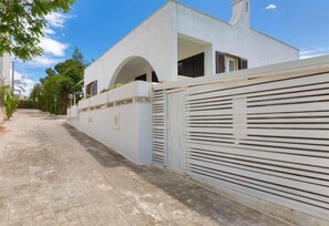 Un bâtiment moderne à la façade blanche, doté d’une entrée sécurisée par un portail et d’un chemin pavé.