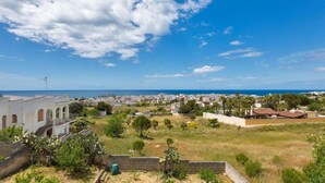 A coastal town with a view of the sea, featuring white buildings with arches, a grassy area with trees, and a clear blue sky. - 674 Villetta con Vista Mare a Santa Maria al Bagno (Nardò)