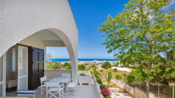 An outdoor balcony with a table and chairs, a view of the sea, and a tree. - 674 Villetta con Vista Mare a Santa Maria al Bagno (Nardò)