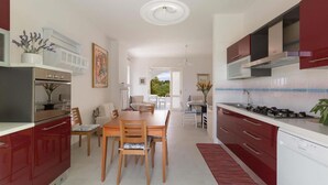 A modern kitchen with red cabinets, a dining area with a wooden table and chairs, and a view of the outdoors. - 674 Villetta con Vista Mare a Santa Maria al Bagno (Nardò)