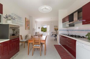 Une cuisine moderne avec des meubles rouges, un coin repas avec une table et des chaises en bois, et une vue sur l’extérieur.