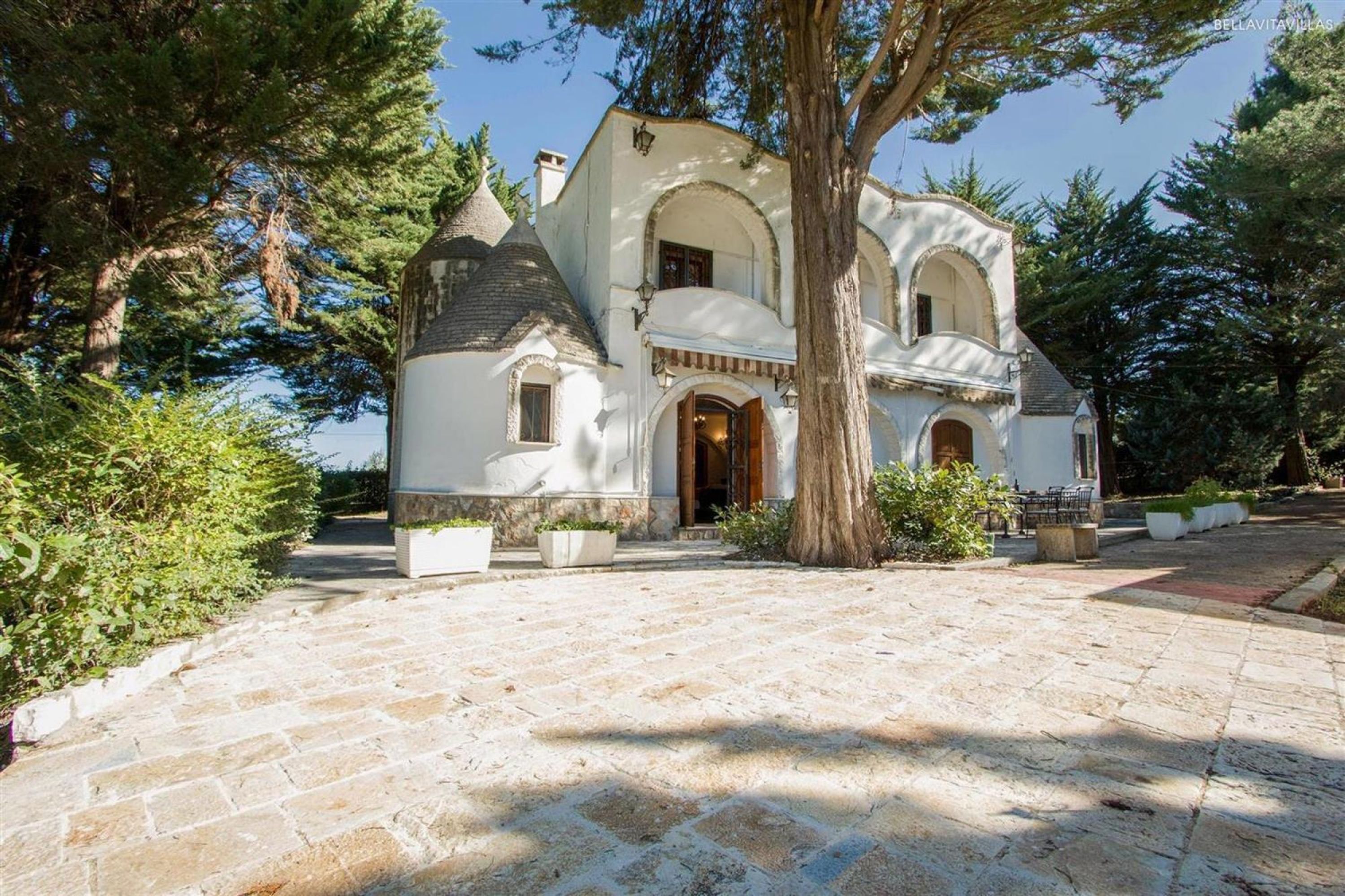 A white building with a large tree in front, stone pathway, and arched windows.