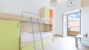 A room with a bunk bed, a ladder, a small table, and a sliding door leading to a balcony. - 857 Appartamento Sirena (Porto Cesareo)