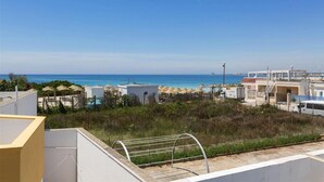 A coastal view with a clear sky, a beach with umbrellas, and a building with a pool. - 832 Villa Belvedere in Porto Cesareo (Porto Cesareo)