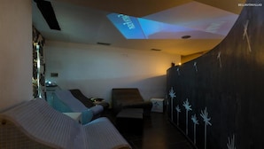 Um quarto com teto arredondado, mesa de massagem, uma cadeira e uma parede com projeção de estrelas.