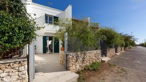 A modern two-story house with a stone facade, a green door, and a fenced garden area. - 2091 Villino Tropical (Porto Cesareo)