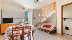 A compact living space with a dining area, sofa, staircase, and laundry area. - 2091 Villino Tropical (Porto Cesareo)