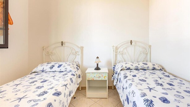 Une chambre à coucher avec deux lits, chacun recouvert d’une couvre-lit à motifs, une table de chevet avec une lampe et un climatiseur fixé au mur.