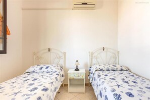 Een slaapkamer met twee bedden, elk voorzien van een beddengoed met een patroon, een nachtkastje met een lamp en een wandairconditioner.
