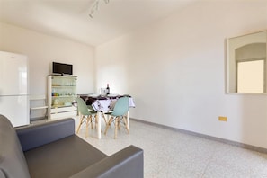 Un salon moderne avec un canapé gris, un coin repas comprenant une table et des chaises, un téléviseur posé sur un meuble et un grand miroir accroché au mur.