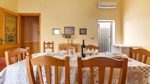 A dining room with a round table, wooden chairs, a vase with flowers, and a wine bottle.