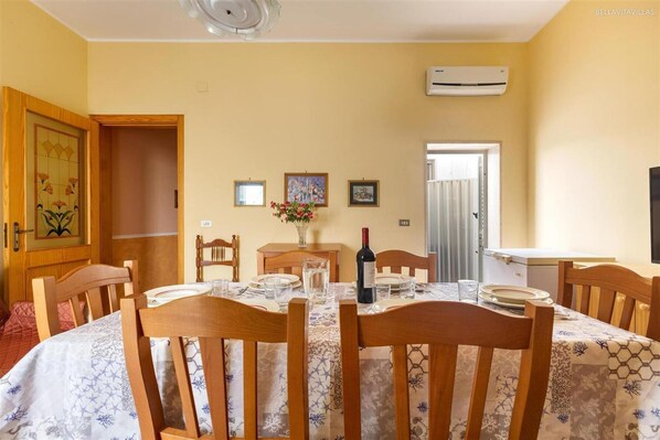 A dining room with a round table set for four, wooden chairs, a vase with flowers, and a bottle of wine.