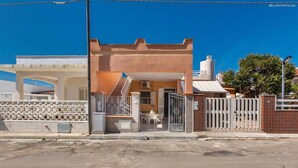 A residential building with a gated entrance, a staircase leading to the upper floor, and a small patio area with a table and chairs.