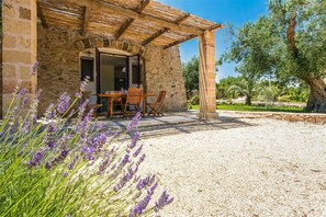 Un edificio de piedra con una pérgola de madera, un patio de grava y plantas de lavanda.