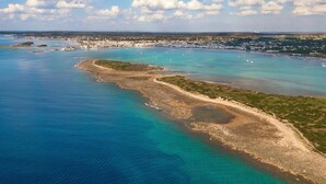 An aerial view of a coastal area with clear blue waters, sandy beaches, and a small town in the background.