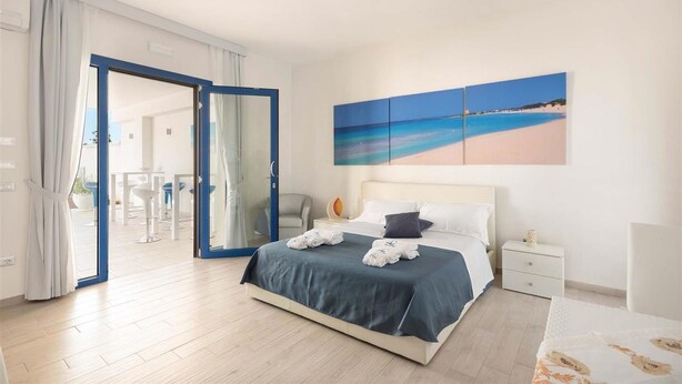 A modern hotel room with a bed, a nightstand, a painting of a beach, and a view of the outdoor area.