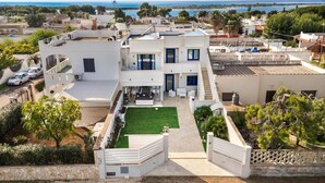 A modern two-story house with a rooftop terrace, a small garden, and a view of the sea.