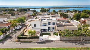 A residential area with a modern two-story house featuring a balcony, a driveway, and a view of the sea.