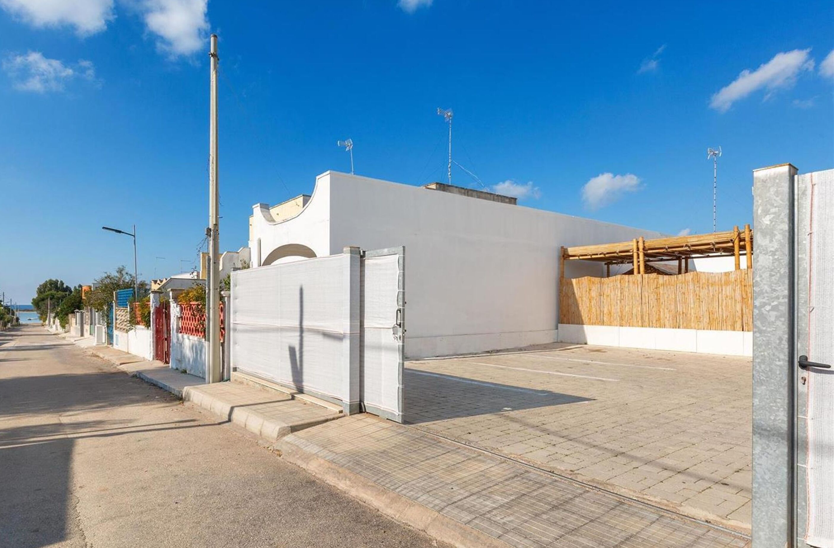 Een straatbeeld met een wit gebouw, een houten omheining en een helderblauwe lucht.