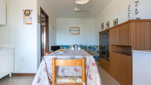 Un coin repas avec une table dressée pour deux personnes, un buffet en bois et un ventilateur de plafond.