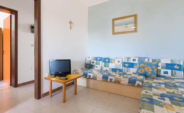 Ein Wohnzimmer mit einer Couch, einem kleinen Holztisch mit Fernseher, einem Kruzifix an der Wand und einem gerahmten Bild.