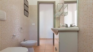 A bathroom with a toilet, bidet, and sink, tiled walls, and a mirror. - 2028 Soledelsud - Monolocale by Barbarhouse (Otranto)