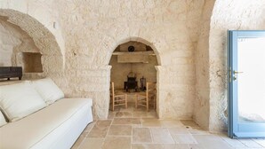 A stone-walled room with a white sofa, a fireplace, and a blue door. - 2410 Tenuta dei Fragni by Perle di Puglia (Ostuni)